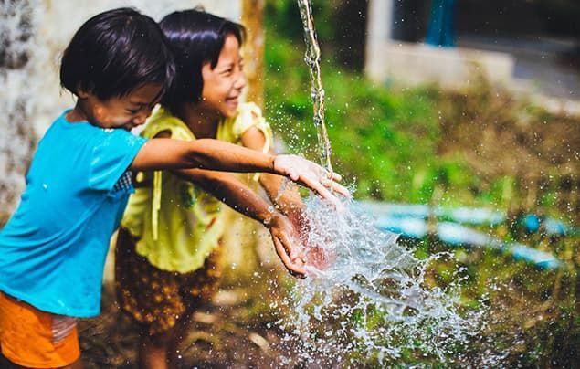 Two young girls play in clean water that spills down from a tap