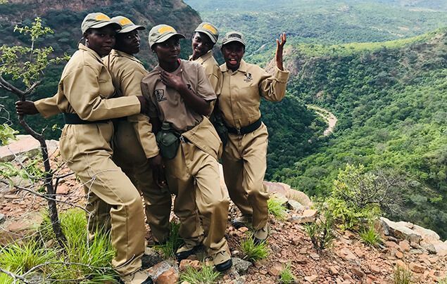female wildlife rangers stand in a group. they are smiling and wearing khakis