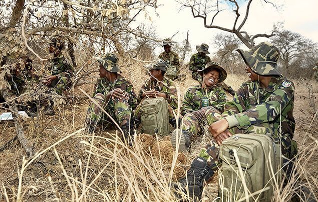 female wildlife rangers sit together on the ground of the savannah, chatting and laughing