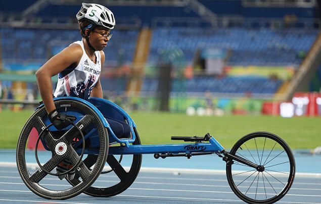 paralympic athlete karé looks focused as she sits in her racing wheelchair, which has two wheels beneath her and one out in front.