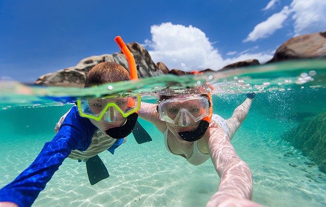 save our seas | two young people snorkelling in a crystal blue sea. They are taking a selfie and smiling at the camera through their masks.