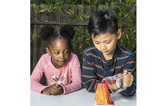 christmas gift guide | two kids watch intently as water is poured into a small red, orange and yellow model of a volcano