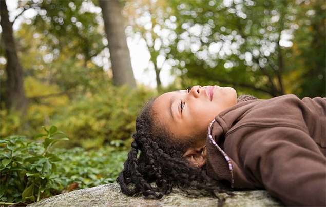 young girl lies on a rock looking up at trees