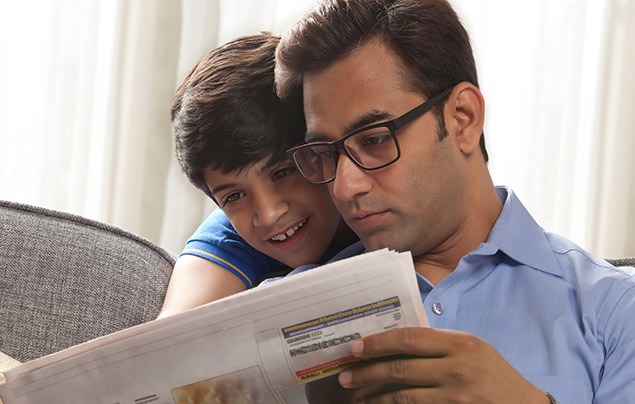 how to spot fake news | a boy looks over his father's shoulder at a newspaper