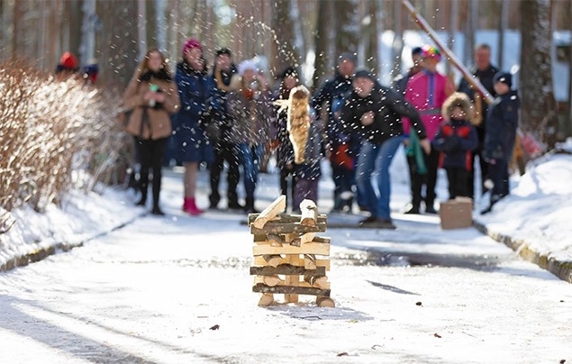winter games for kids | a tower made of wooden logs stands about 3 metres in front of a group of people. There is snow on the ground. One of the people throws a log at the tower. It rockets through the air, snow flying off it as it travels towards the tower.