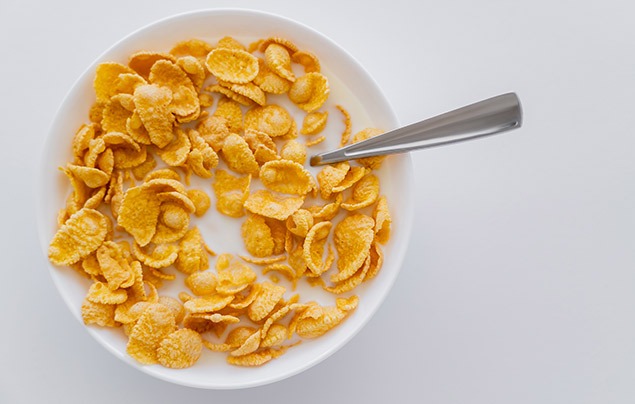 april fools' pranks | a white bowl of orange cornflakes covered with milk, with a spoon sticking out