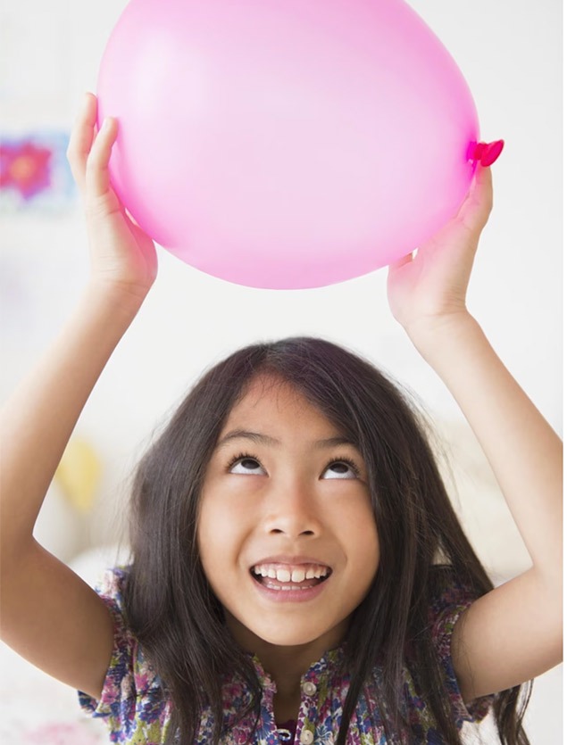 a young girl holds a pink balloon over her head