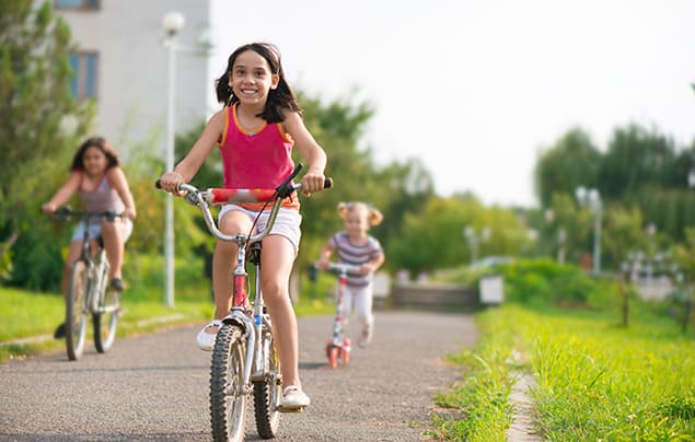 sustainable development goals | a young girl rides her bike through a green park with a high rise building in the background