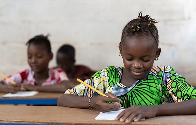 sustainable development goals | a young girl in a green dress practises writing with a pencil