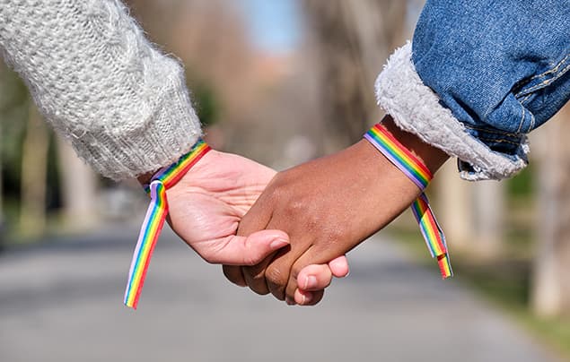 sustainable development goals | two people hold hands. There are rainbow patterned bracelets on their wrists - the symbol of the LGBTQIA+ movement