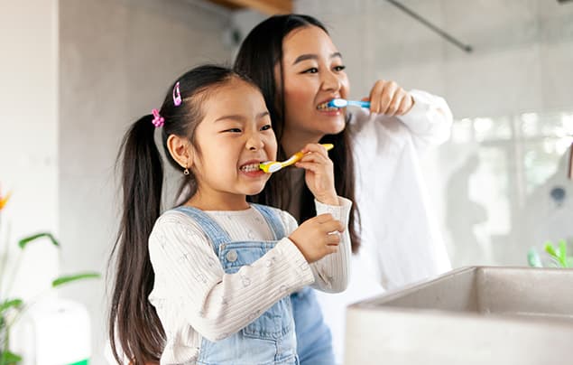 sdgs | a woman and her daughter brush their teeth in front of a mirror