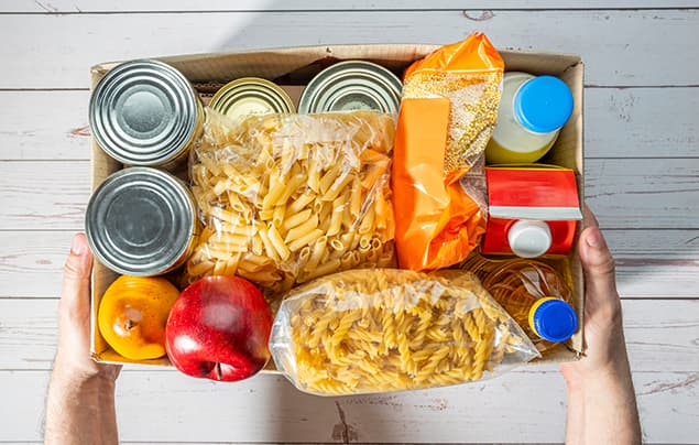 sdgs | a box for a food bank, containing dried pasta, tinned foods, cartons of long-life milk and oil, and a fresh apple