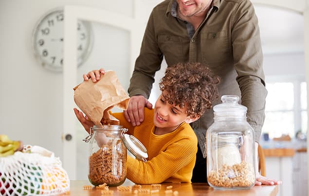 sdgs | a young boy in a yellow top pours dried pasta from a brown paper bag into a glass jar