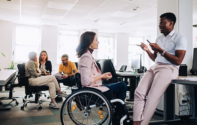 sdgs | a woman using a wheelchair chats to her colleague in their office