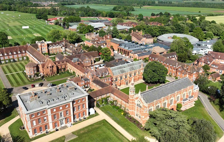 Aerial view of Radley’s large, historic school campus with red-brick buildings, green lawns, sports fields, and tree-lined paths, surrounded by countryside.