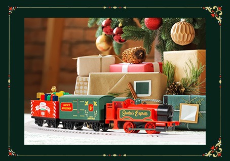 A toy train in front of a stack of Christmas presents and a Christmas tree. 