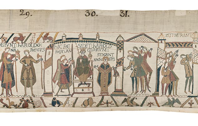 Medieval tapestry scene showing figures in robes, some seated and others standing, with text above and architectural elements in the background. The style is illustrative, with muted colours and detailed embroidery.
