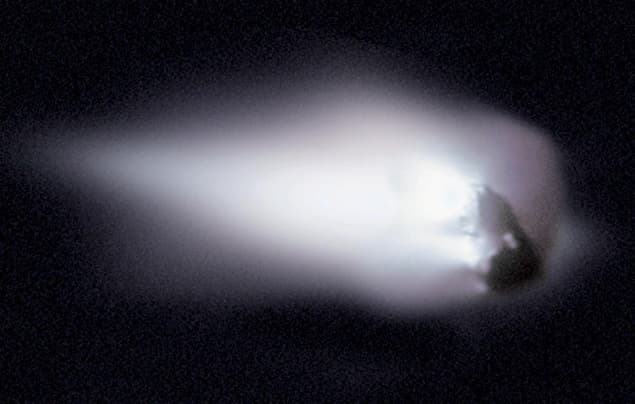 A bright, glowing object with a white tail moves through a dark sky, resembling a comet or meteor travelling in space.